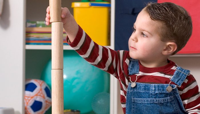 Young boy building tower with cylindrical wooden blocks