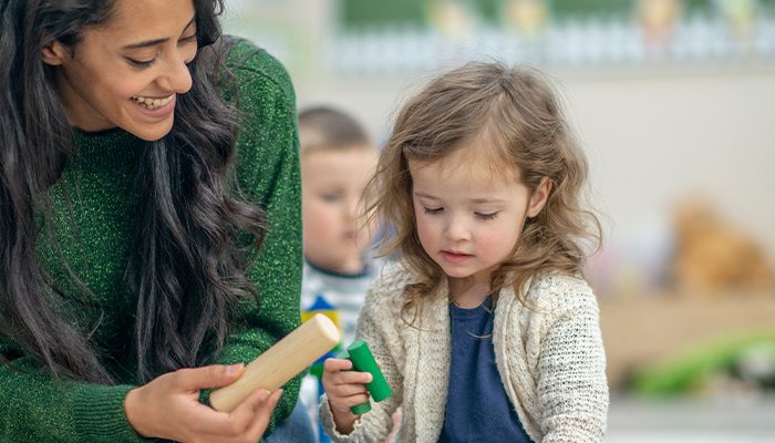 Female teacher hands a wooden block to a young child